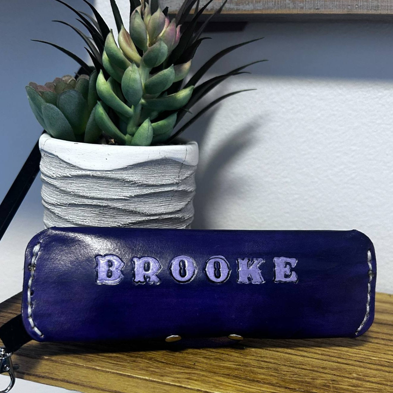 Custom leather case by Tanné & Co. featuring the customers name (BROOKE) stamped with painted detail in lilac purple on a dark hand-dyed purple leather base with white stitching. This handcrafted personalized eyewear case showcases the brand’s attention to detail and custom leatherwork, ideal for unique styles or one-of-a-kind accessories.